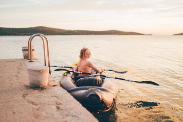 Teenage boy on bright yellow inflatable kayak preparing for evening ride by Adriatic Sea harbor near Sibenik, Croatia. Family vacation, outdoor adventure, travel lifestyle concept image.