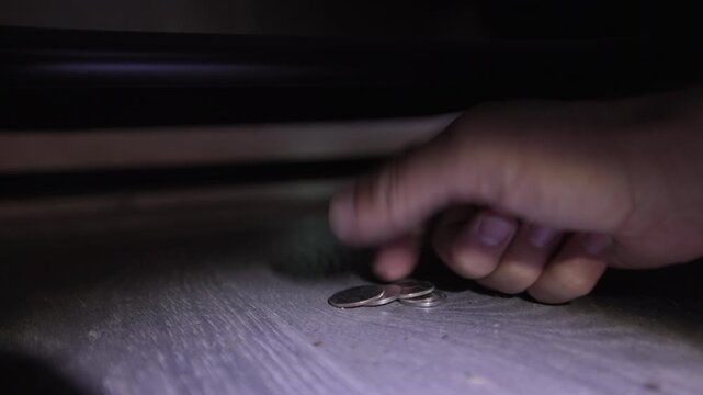 A realistic moment captured as a person uses a flashlight to search under a couch and discovers loose coins. Visible dust and worn couch springs add to the authenticity of this everyday scene.