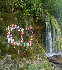 Wire heart with colorful ribbons at a waterfall in a symbolic style in green and multi-colors...
