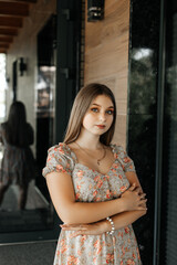 Girl in a floral dress against the background of a house wall with a mirror behind her