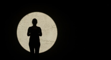 A silhouette of a person stands against a large, illuminated circular shape, creating a striking contrast with the dark background.