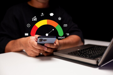 A person is using a smartphone next to a laptop, with a digital gauge indicating performance levels, symbolizing connectivity and technology usage.