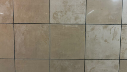Worn beige square tiles with dark grout lines forming a geometric grid pattern.