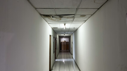 Long Empty Hallway with Damaged Ceiling and Fluorescent Lights in an Old Building.