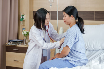 Asian female doctor using stethoscope to check breathing and heartbeat of female patient on...