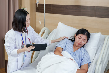 Asian female patient crying in hospital bed receiving emotional support from female doctor with...