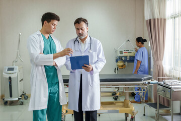 Multiracial male doctors discussing patient treatment plan using blue clipboard in hospital...