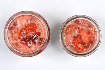 A top-down shot of two glass jars filled with homemade strawberry jam, showing the rich texture and color against a plain gray background