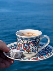 Traditional Turkish Coffee cup is held in a han dwith piece of sugar on blue sea background in sunny day
