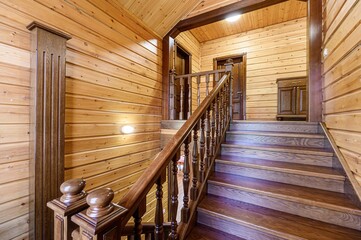 Warm wooden interior features a staircase with dark wood steps and balustrade. Light wood paneled walls and ceiling create a cozy, rustic atmosphere