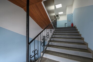 Interior shot of a staircase with blue walls and a black metal railing. The stairs are tiled in gray