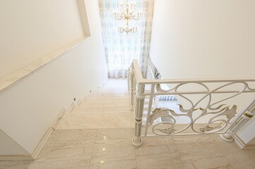 Elegant staircase with marble steps and ornate white railing, bathed in soft light. A chandelier is...
