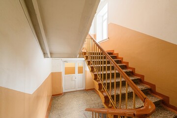 Indoor staircase with orange/white walls, leading up to a window. Handrail is wood and metal. Door...