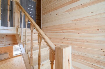 bright, natural wood interior features a staircase with crafted wooden railings and balusters. The...