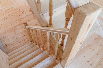 Wooden staircase with light-colored wood, seen from above. Shows details of the balusters, handrail, and wood grain