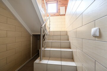 staircase ascends with tiled steps and a stainless steel railing. Walls are covered in...