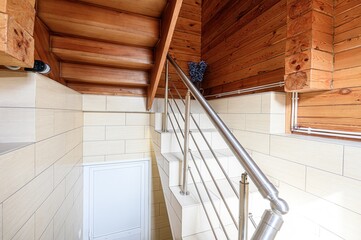 Indoor stairwell with wooden steps, tiled walls, and a stainless steel railing. A small white door...