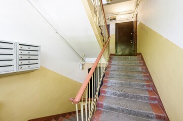 Stairwell with mailboxes, leading up to a dark door. Walls are painted in two-tone fashion