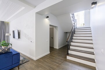 Modern home interior with white walls, wood floors, a blue sofa, a staircase, and sleek lighting fixtures