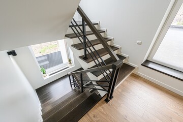 overhead shot of modern stairs with dark wood steps, white risers, and black metal railings in a bright, minimalist interior with wooden floor