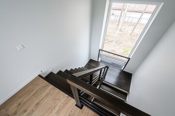 Staircase with dark wood steps and metal railing, leading to a light wood floor and a large window....