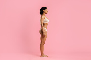 Side profile of fit young African American woman in beige underwear on pink background. Healthy...