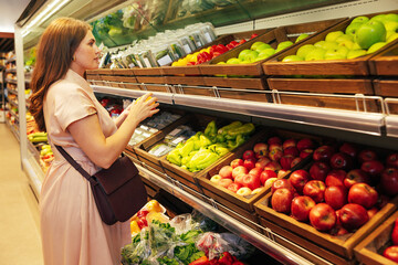 Side view of a young female at the shelves in the grocery store, and decided what to buy