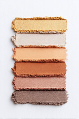 Fototapeta premium Colorful swatches of eyeshadow in natural tones arranged horizontally on a white background, perfect for makeup enthusiasts and beauty professionals seeking inspiration