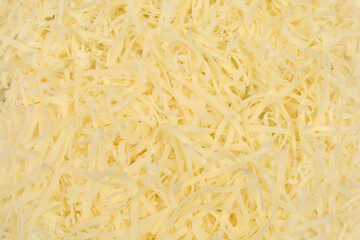 A full-frame close-up of a pile of shredded or grated pale yellow cheese, showcasing its texture