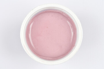A top-down, close-up shot of a small cup of fruit yogurt, showcasing its smooth texture and subtle pink color against a white background