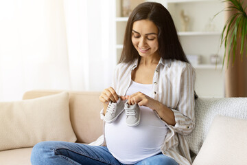 Pregnant woman looking down and smiling at baby shoes on her belly. Shows maternal connection, joy...