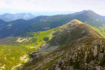 A scenic view of a mountain ridge covered in green and rocky terrain under a bright sky.