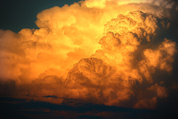 A massive, glowing cumulus cloud formation illuminated by the golden light of the sun, possibly at...