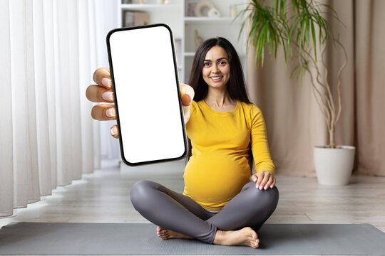 Pregnant woman holding blank phone screen towards camera while smiling. Perfect for mobile apps, telemedicine or maternity-related promotions, mockup