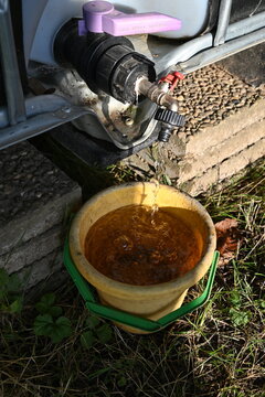 Gro&szlig;er IBC-Container zur Regenwassersammlung im Garten, montiert auf Steinen mit Auslaufhahn und Eimer &ndash; nachhaltige Wassernutzung f&uuml;r Gartenbew&auml;sserung.