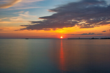 Fototapeta premium Dramatic Sunset Over Calm Sea with Silhouetted Harbor - Peaceful Evening Sky