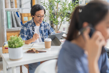 Cheerful Asian businessman with positive thinking and confidence sits at her desk, working in a...