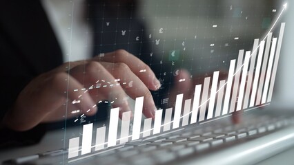 A business professional types on a keyboard while analyzing digital graphs that illustrate growth...