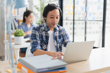 Cheerful Asian businessman with positive thinking and confidence sits at her desk, working in a...