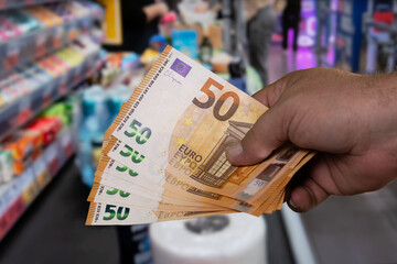 Hand holding multiple fifty euro banknotes in a retail store during a busy shopping day