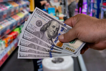 Person holding multiple hundred dollar bills in a retail store while making a purchase during the day