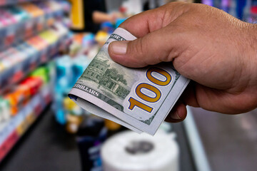 Hand holding a hundred dollar bill in a busy store checkout aisle during a shopping trip