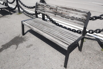 Old wooden bench surrounded by a chain barrier near a roadway on a sunny day showcasing urban...