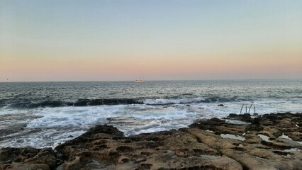 Rocky shoreline at sunset with waves crashing onto the rocks  