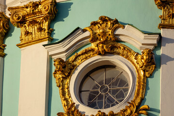 Gilded baroque ornament on the facade of St. Andrew's Church in Kyiv, Ukraine. Two cherubs frame a circular window, with an ornate Corinthian capital visible on the left.