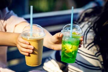Girl's hands offering two transparent plastic cups with straws - one with iced coffee, the other...