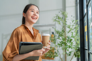 smart casual confident small business asian female woman standing hold tablet coffee cup smiling...