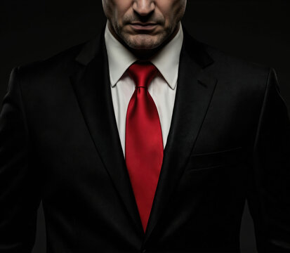 Confident businessman stands against dark background with sharp red tie. Classic black suit, white shirt, formal attire exude power, authority. Steady gaze, strong stance convey leadership, success.