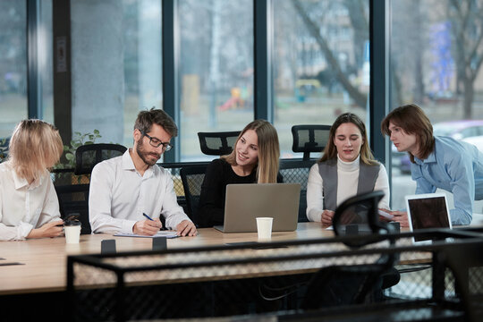 A group of people are sitting around a table with a laptop