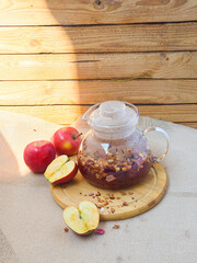 Fruit autumn tea in a glass teapot on a wooden board on a white background, red apples are lying nearby. autumn. autumn mood. coziness
